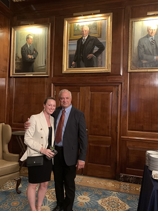 Bill Angresano standing with a companion in a portrait-lined room